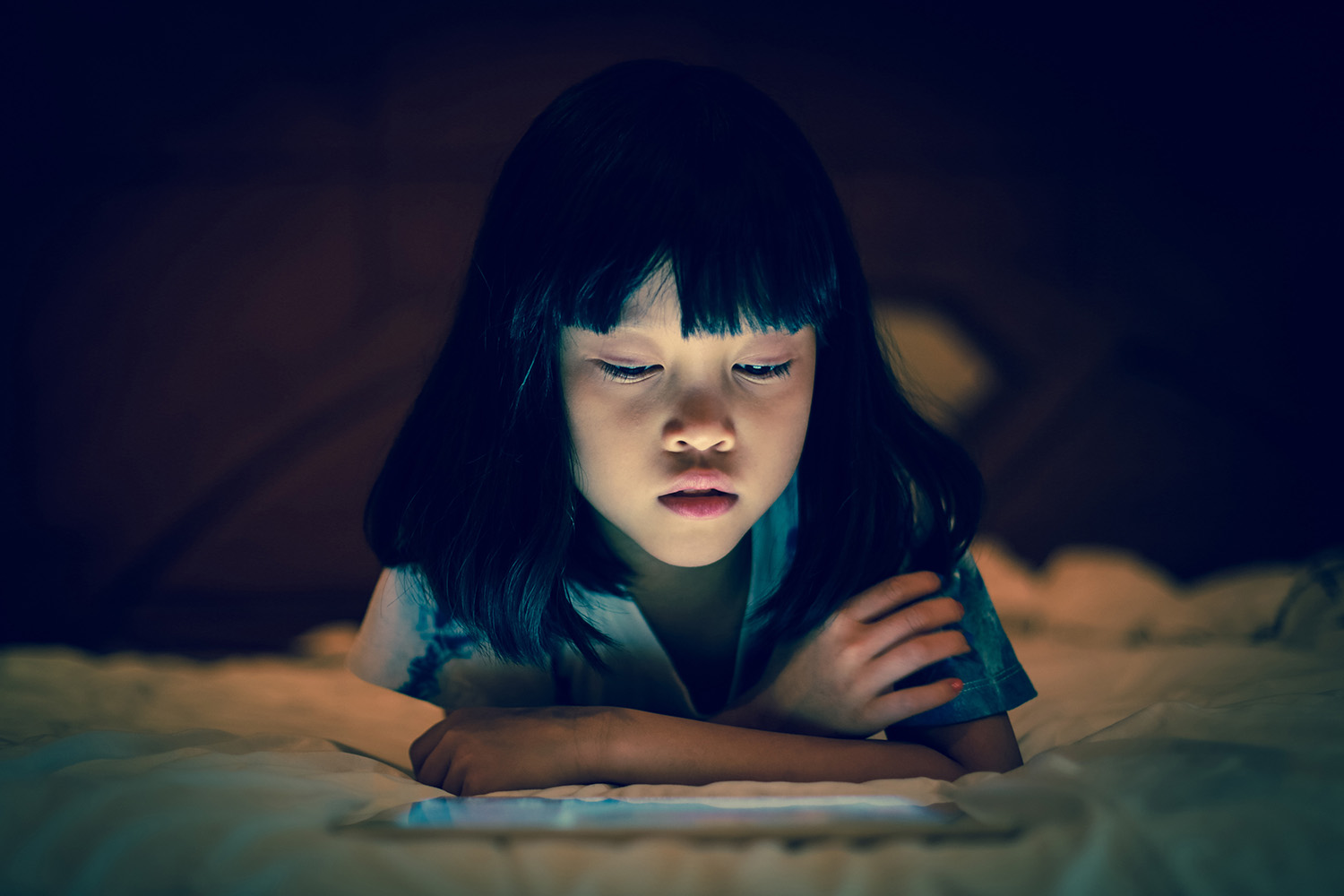 Mädchen schaut auf ein Tablet; Umgebung dunkel